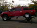 1985 Ford Bronco - A red pickup truck with V8 TITAN badging is shown on a lift.