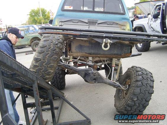 Off-road truck rear axle and suspension with large tires, another truck in background