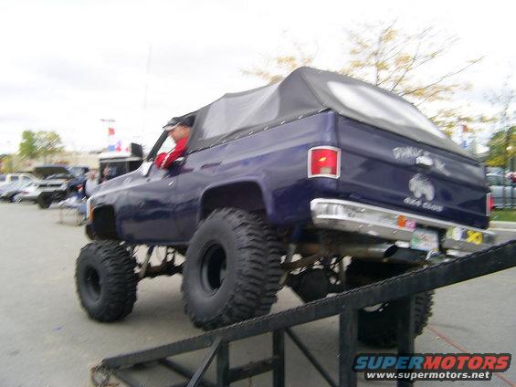 Purple lifted SUV with a soft top, driving up a ramp, with "Damage Inc 4x4 Club" decal on the rear