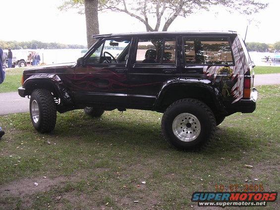 Black lifted Jeep Cherokee XJ with flame graphics by a lake