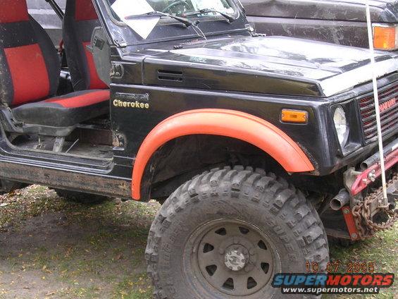 Suzuki Samurai with red and black seats, orange fender flares, and large off-road tires. Another vehicle is partially visible behind it