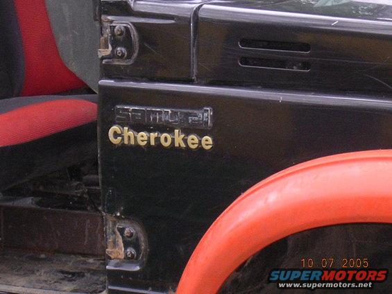 Close-up of black Suzuki Samurai side panel with gold 'Cherokee' badge and red seat visible
