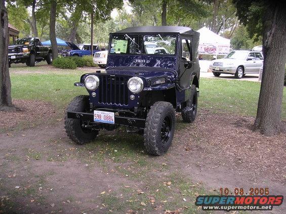Dark blue Willys Jeep with black soft top, front view, large off-road tires, and license plate 598 0884