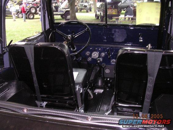 Interior view of a vintage Jeep with dark seats, steering wheel, and dashboard gauges. Other vehicles visible outside