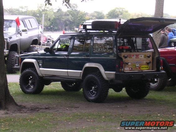 1995 Jeep Cherokee, dark green, lifted with off-road tires, roof rack, open tailgate showing storage boxes