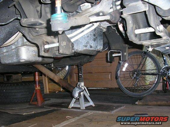 Undercarriage of a vehicle supported by jack stands, with a bicycle wheel visible on the right