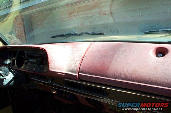 Dashboard of a pickup truck with a red dash pad, radio, and vents. Windshield wipers visible through the dusty windshield