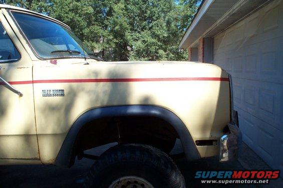 Cream-colored Dodge pickup truck with red stripe and 'Trail Duster' badge parked next to a garage