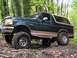 1995 Ford Bronco - A lifted 1995 Ford Bronco navigates a muddy trail surrounded by trees.