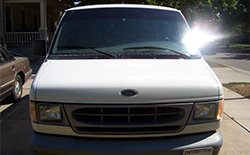 White Ford Econoline van, front view. Sun glare on windshield