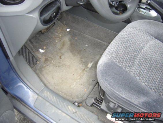 Interior of a car showing a dirty floor mat with 'SANTA FE' visible, driver's seat, and steering wheel