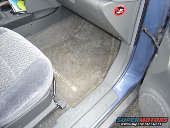 Car interior showing a blue door, grey carpet, and a grey fabric seat. A "no smoking" sticker is visible on the dashboard