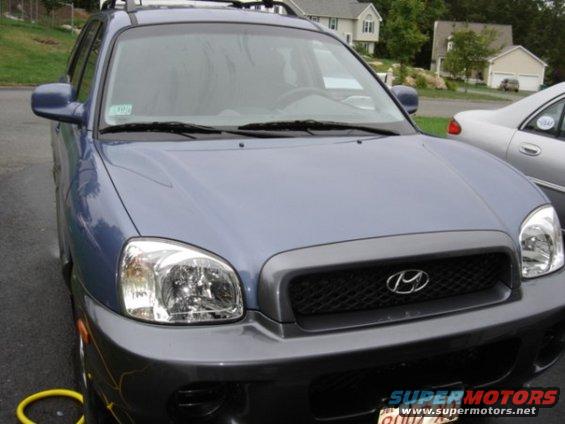 Blue Hyundai Santa Fe SUV front grille and headlights, parked next to a silver sedan