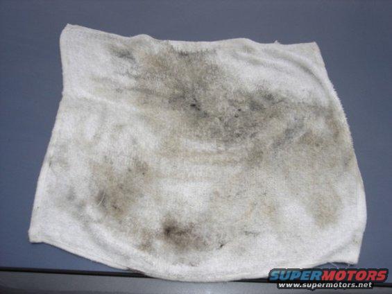 dirty white rag with oil stains on a gray surface. There's a watermark at the bottom right