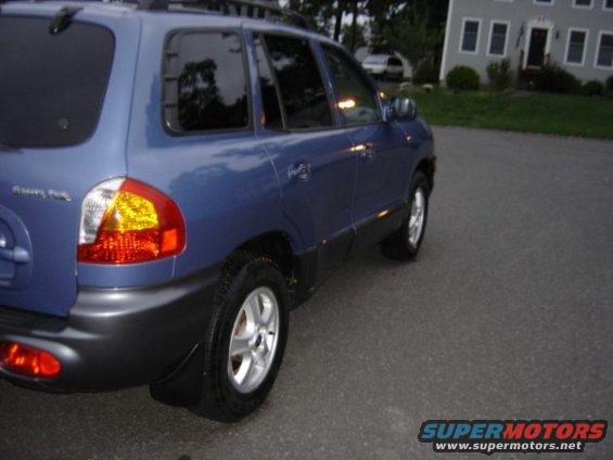 Rear quarter view of a blue Hyundai Santa Fe parked on a street. The vehicle has tinted windows and a roof rack