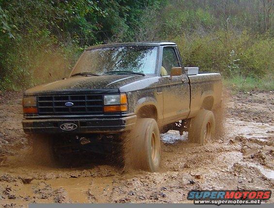 Black Ford Ranger kicking up mud while driving off-road. The truck has a toolbox in the bed