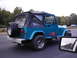 1979 Ford Bronco - Teal Jeep Wrangler YJ with soft top and spare tire on rear bumper is seen from the side while driving.