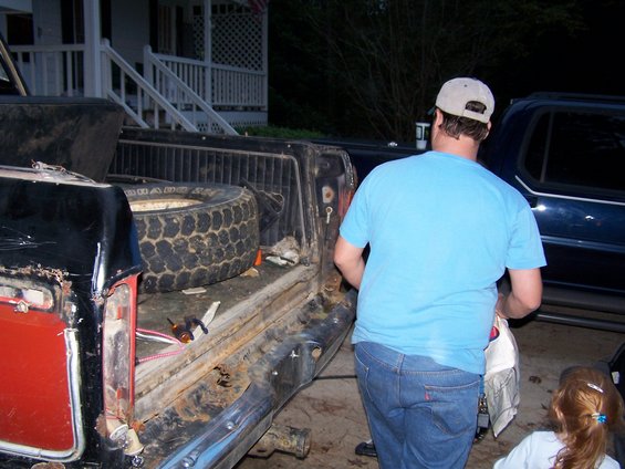 man loading stuff into old pickup truck bed, spare tire visible