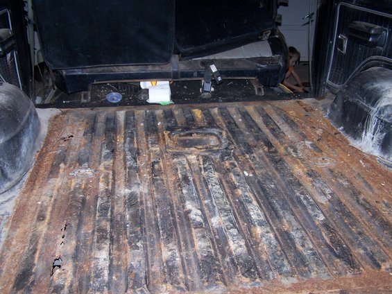 Rusted ribbed floor of a truck bed, with seats visible in the background