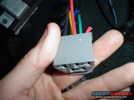 Hand holding gray wiring harness connector with multiple colored wires coming out