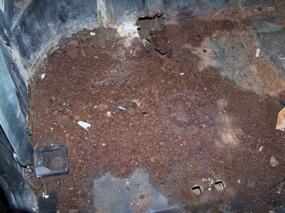 Rusted interior floor with debris and a black plastic trim piece