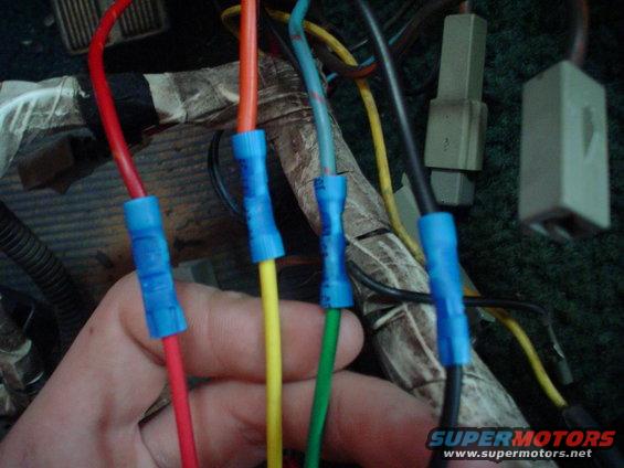 Hand connecting wires with blue crimp connectors in a vehicle's wiring harness