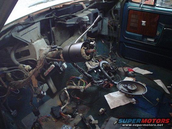 Car interior torn apart, wires everywhere, steering column removed, door panel visible