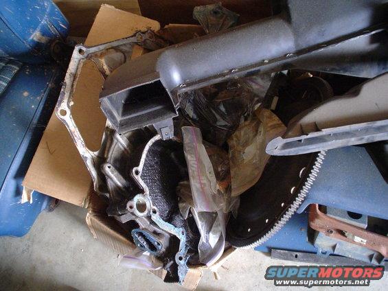 Pile of engine parts including a gasket, intake manifold, and flywheel