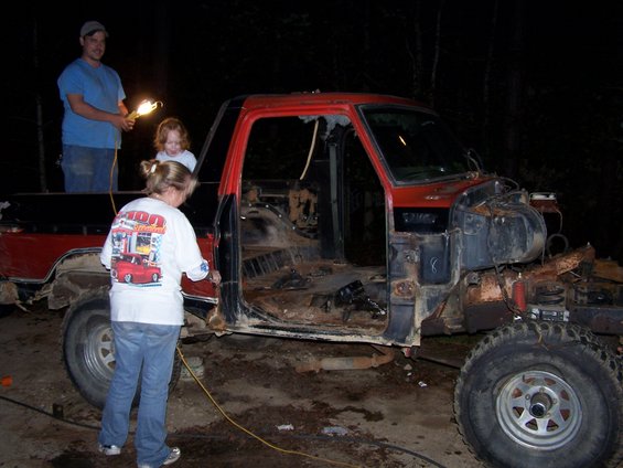 people working on a stripped-down red and black pickup truck at night