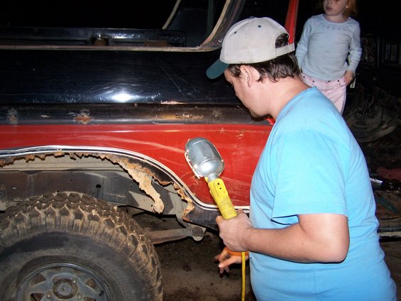 Man with work light inspecting heavily rusted fender of a 1979 Ford F-150
