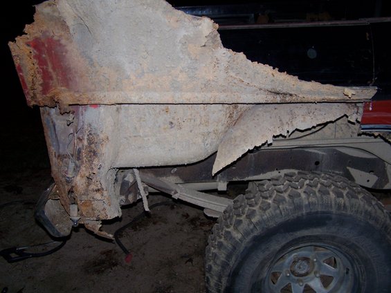 Heavily rusted truck quarter panel with visible leaf spring and tire