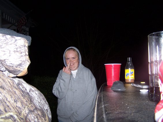 Woman in a grey hoodie picking her nose, standing next to a red cup and a bottle of Yoohoo
