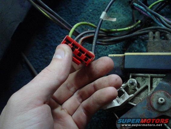 Hand holding red electrical connector near vehicle wiring harness
