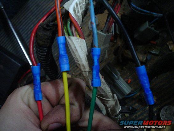 Hand holding red and yellow wires with blue connectors, near other wires and electrical components