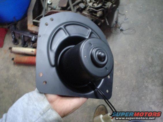 Hand holding black blower motor assembly with wires