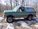 1989 Ford Bronco - A green Ford Bronco with a tan top navigates a rocky trail.