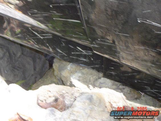 Scratched black vehicle body panel above rocks. Watermark reads OCT 8 2005 SUPERMOTORS.NET