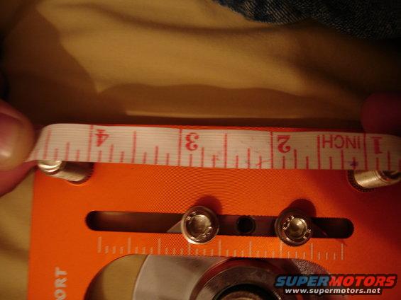 Tape measure showing 2 to 4 inches held over an orange tool with screws and markings