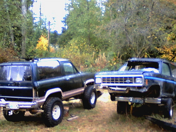 Two dark-colored Ford Bronco II SUVs parked outdoors, one with its front end elevated
