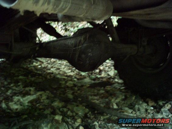 Underside of a vehicle showing a rear axle and exhaust pipe, with a tire visible on the right