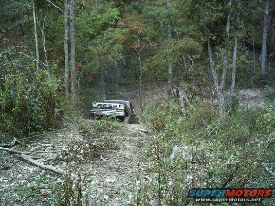 1986 Ford Bronco driving on a wooded dirt trail