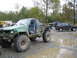1990 Ford Bronco - Heavily modified green Toyota pickup truck with oversized tires and a custom roll cage sits in a muddy area, with other vehicles visible in…