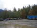 1990 Ford Bronco - A collection of off-road vehicles are gathered in a muddy area, with a large blue container and trees in the background.