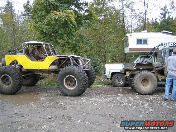 Yellow buggy with huge tires parked next to a tow truck with a camper shell