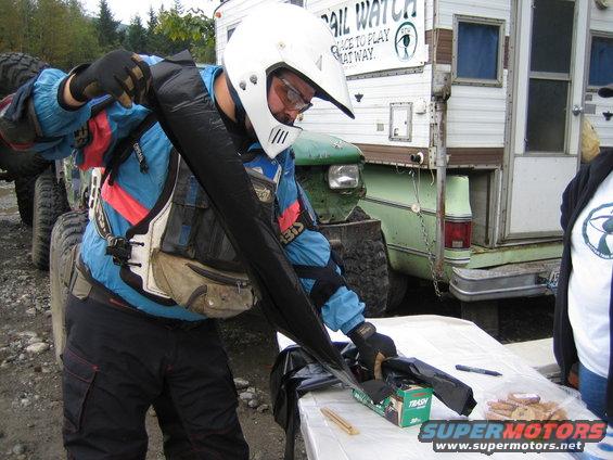 Person in helmet and gear next to green truck and camper, preparing for off-road activity