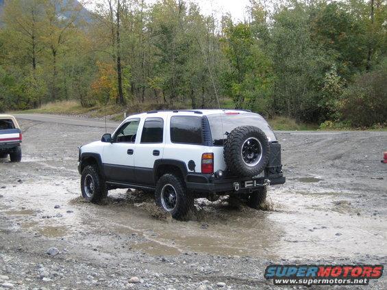 White and black SUV driving through mud puddle, another SUV in background