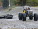 1990 Ford Bronco - A custom off-road vehicle tows a mangled car chassis across a muddy, gravelly surface.
