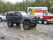 1990 Ford Bronco - A heavily modified Ford Bronco sits in a muddy lot next to a U-Haul truck and trailer.