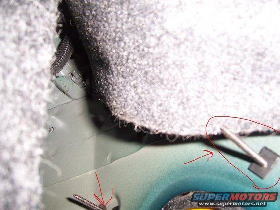 Car interior floor with carpet trim, metal panel, and a screw. A red circle highlights a metal clip