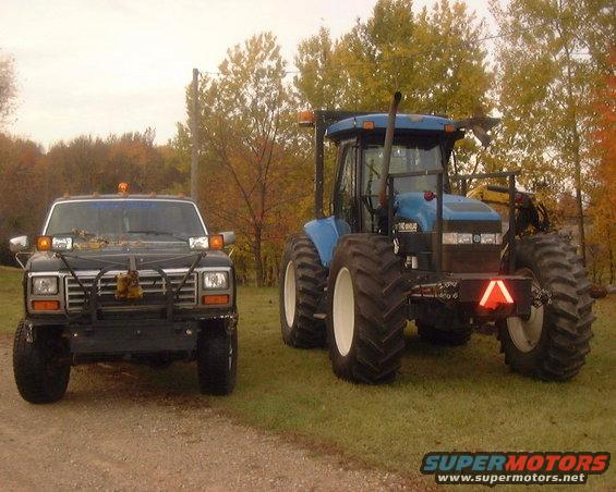 Black Ford F-150 with a brush guard and auxiliary lights, parked next to a blue tractor